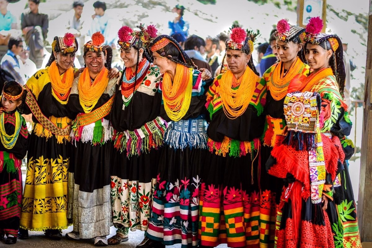 Kalash women performing circle dance at a festival, wearing traditional black robes and elaborate headdresses.