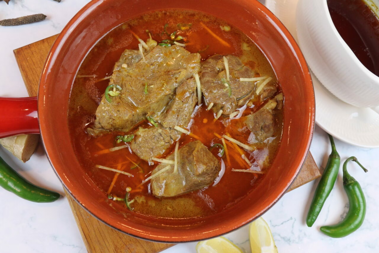 Nihari in a traditional serving bowl, garnished with ginger julienne, fresh coriander, and a slice of lemon